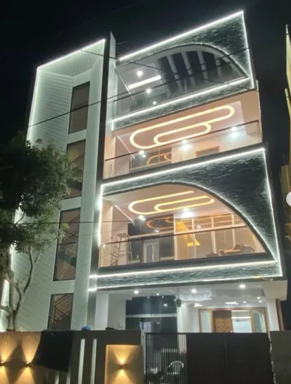 Completed residence façade photographed at night, with illuminated arched feature panels, frameless glass balconies and linear cove lighting