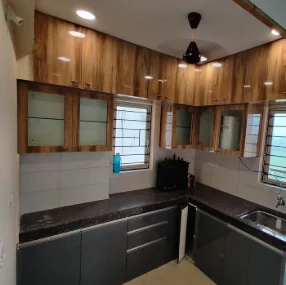 Completed L-shaped modular kitchen with woodgrain laminate wall cabinets, graphite base units and a dark granite counter